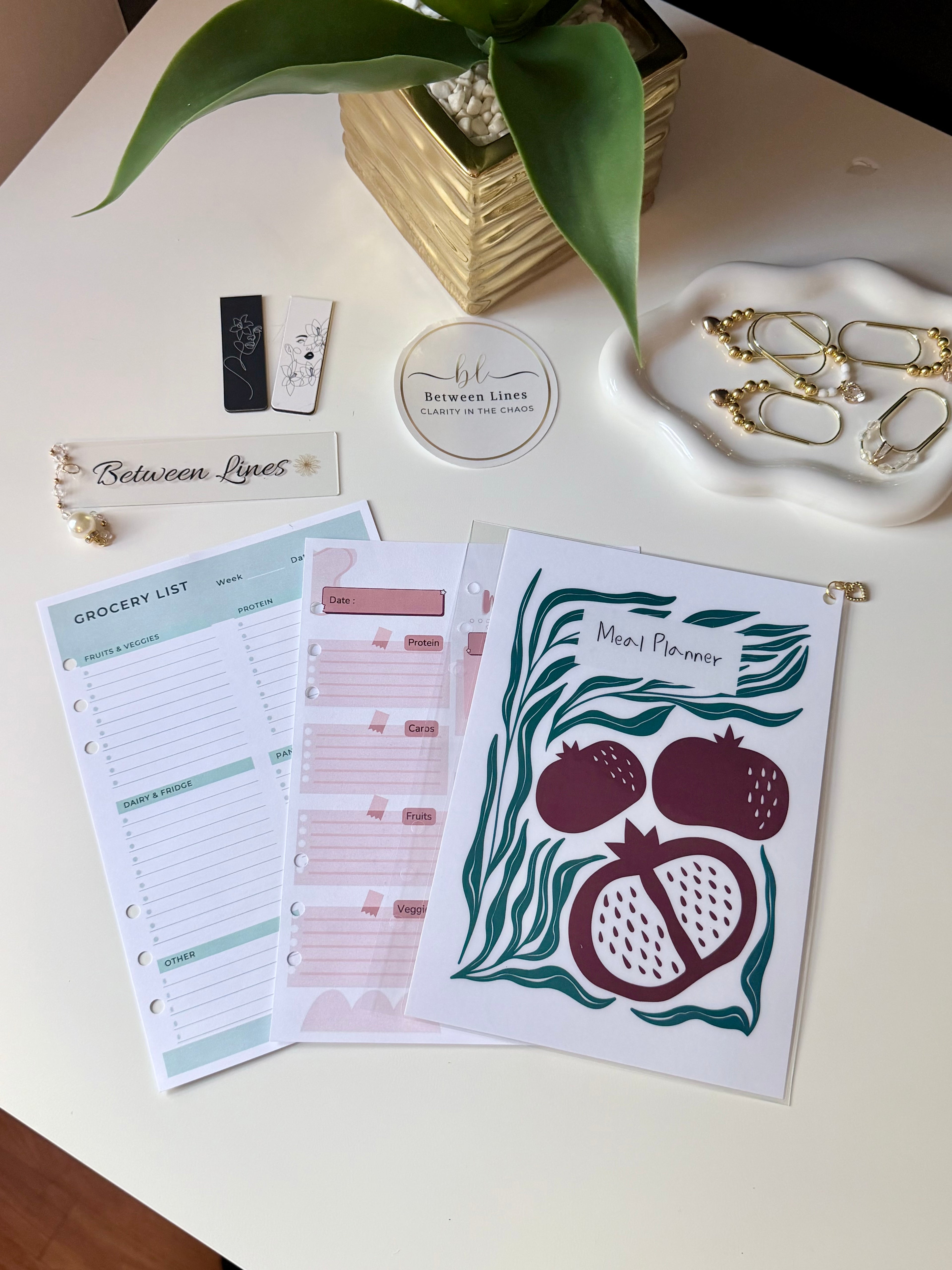 Between Lines Meal Planning Sheets flat lay showing weekly meal planner, grocery list, and decorative cover page with pomegranate illustration